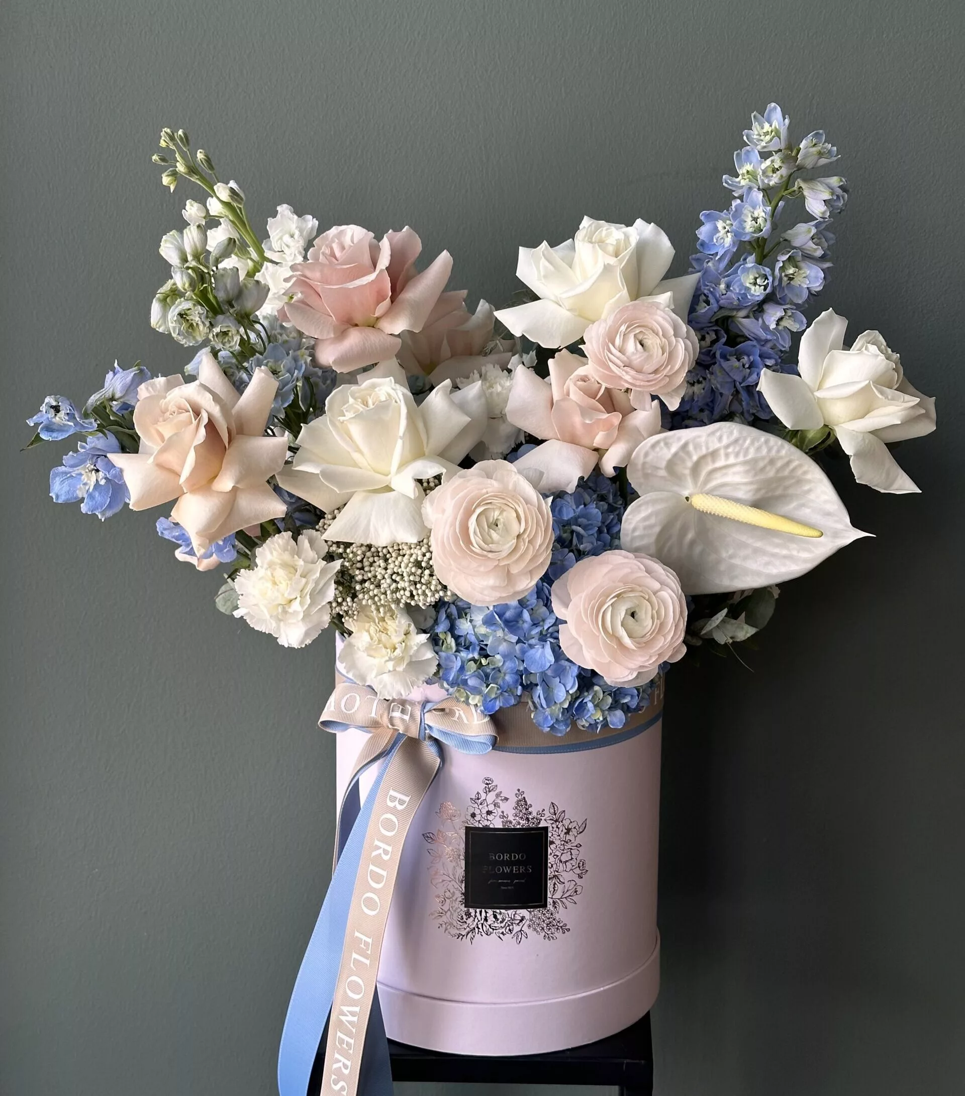 Blue Bell - Bordo Flowers The "Blue Bell" box arrangement is a charming floral display designed to celebrate new beginnings. Available in small, medium, and large sizes, this arrangement features a delightful mix of light blue, beige, and white flowers. Perfect for welcoming a newborn baby boy or any male celebration, the soft color palette evokes a sense of tranquility and joy. Each box is beautifully curated, creating a stunning centerpiece that brings warmth and elegance to any occasion. Whether given as a gift or used as decor, the "Blue Bell" arrangement is sure to make a heartfelt impression.